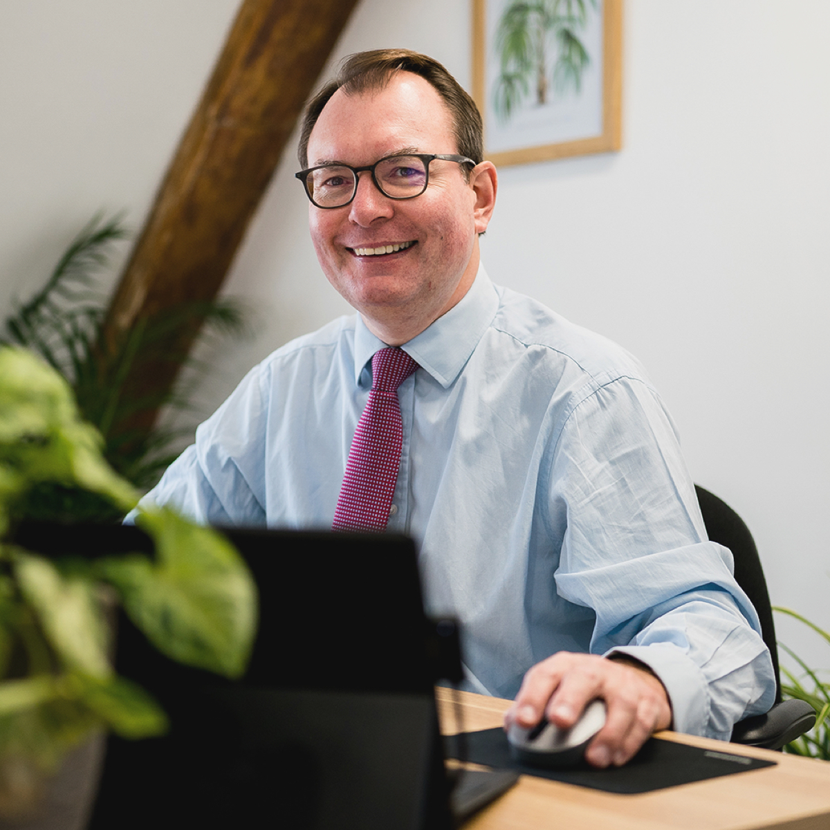 Paul Willans smiling while he works at his desk at AJB Wealth