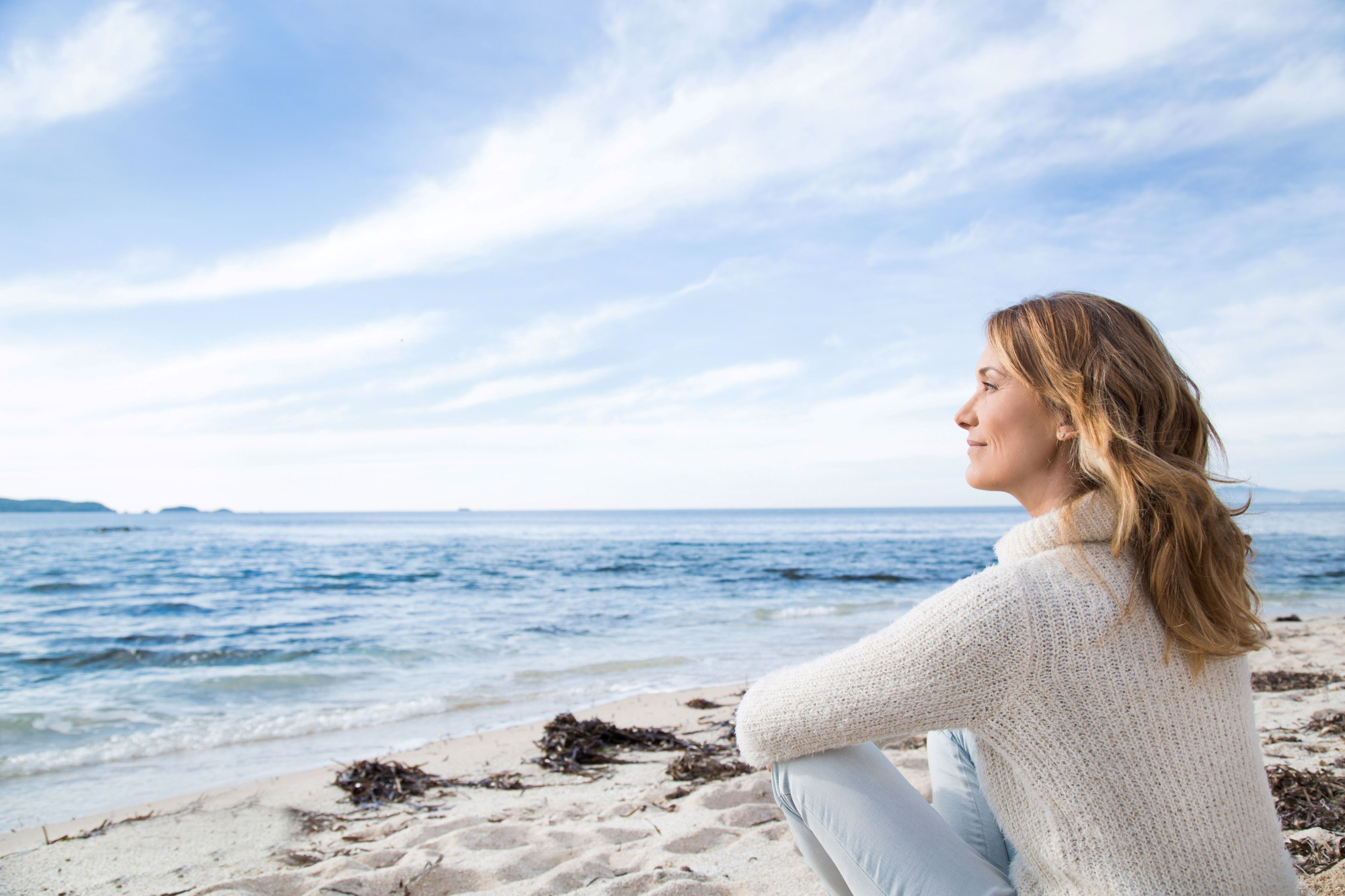 This image shows a woman sitting pensively on the beach, looking out to sea